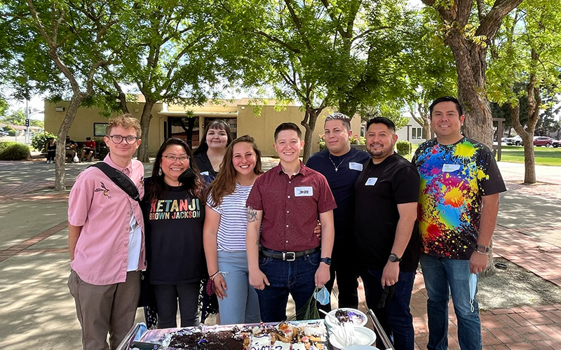 group of young adults stand together in the church courtyard in front of a birthday cake