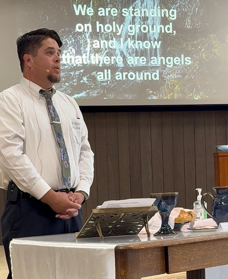 Pastor Mark standing at a table with Holy Communion bread and goblet